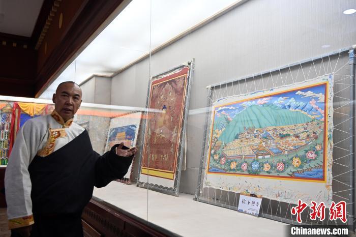 圖為交巴加布展示以拉卜楞寺為主題的唐卡作品。交巴加布不僅繼承了傳統(tǒng)唐卡技藝，更在創(chuàng)新中展現(xiàn)了個人特色。他結合現(xiàn)代審美和繪畫技巧，使作品既保留了傳統(tǒng)的韻味，又具有鮮明的現(xiàn)代氣息。這種獨特的藝術風格使他的作品在眾多唐卡中脫穎而出，成為藏族民眾和藝術愛好者爭相收藏的藝術珍品。九美旦增 攝

